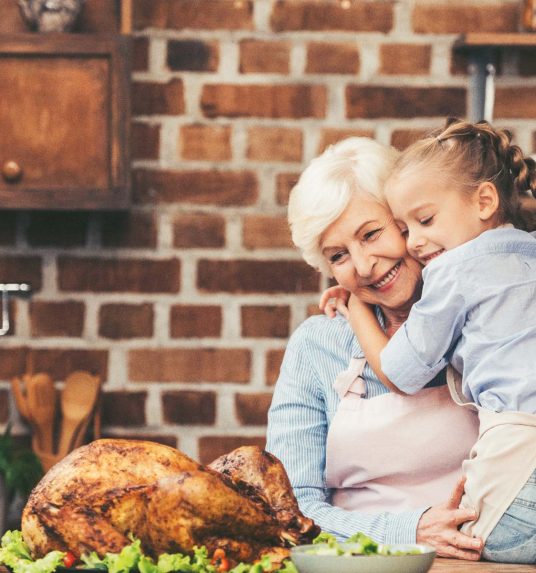A grandmother hugs her granddaughter in the kitchen.